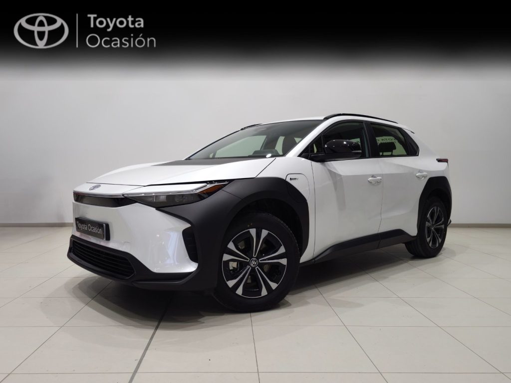 White Toyota compact SUV in a showroom, angled three-quarter front view with black cladding and large alloy wheels, showroom banner reads 'Toyota Ocasión' in the background.