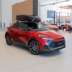Toyota CHR 2026 GR SPORT 140H ID: 8756 Red Toyota C-HR SUV on display in a bright showroom with a black roof cargo box mounted on top.