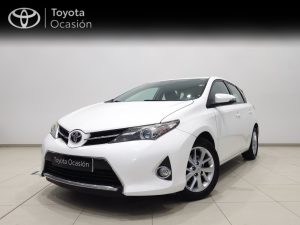 Front three-quarter view of a white Toyota sedan in a showroom, with 'Toyota Ocasión' banner in the background, highlighting the car's grille and headlights.