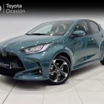 Front three-quarter view of a teal Toyota hatchback in a showroom, with a Toyota Ocasión banner in the background.
