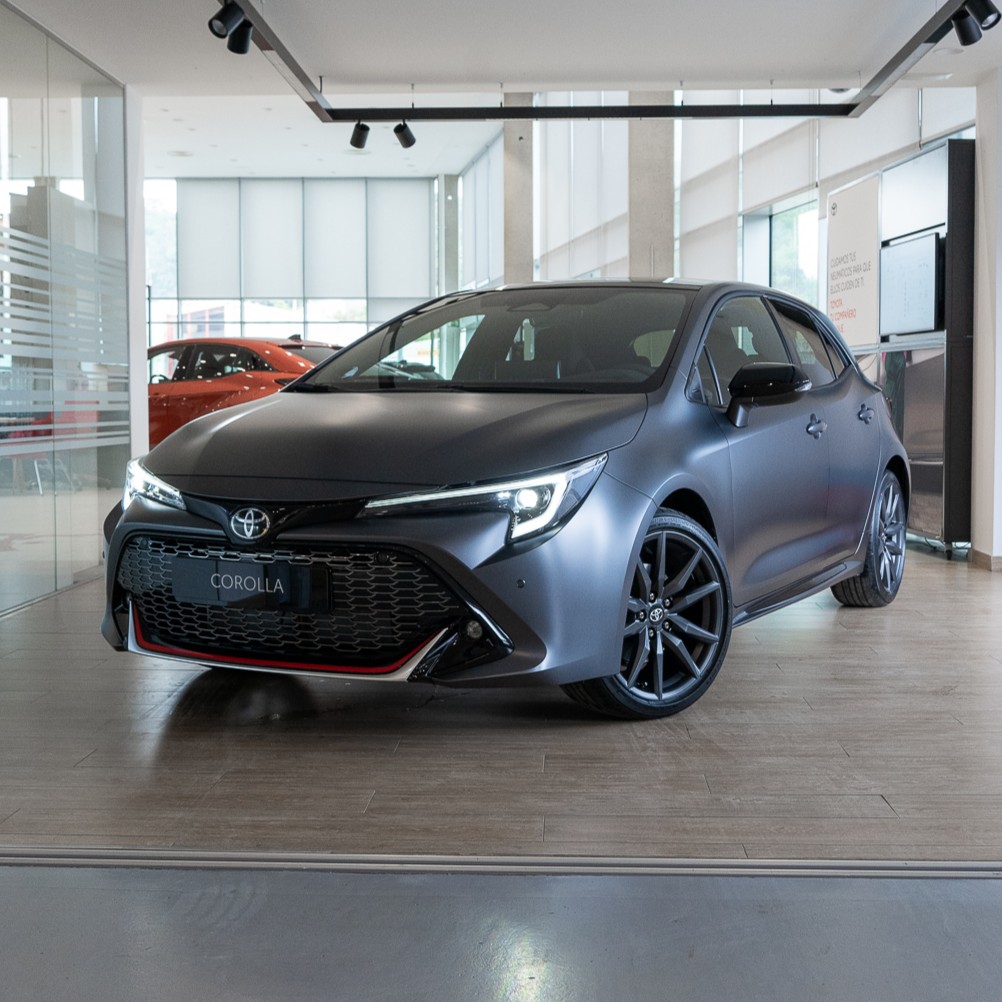 Matte blue-gray Toyota Corolla sedan on a showroom floor, front three-quarter view.