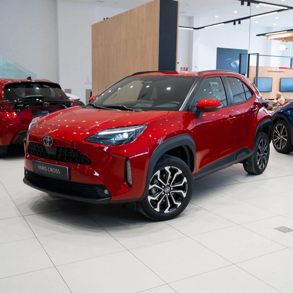 Red Toyota Yaris Cross SUV on a showroom floor, front three-quarter view with another car in the background.