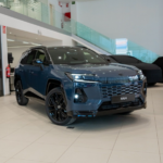 Blue Toyota RAV4 on a dealership showroom floor, angled front view with bright lighting and glossy finish.