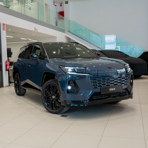 Blue Toyota RAV4 on a dealership showroom floor, angled front view with bright lighting and glossy finish.