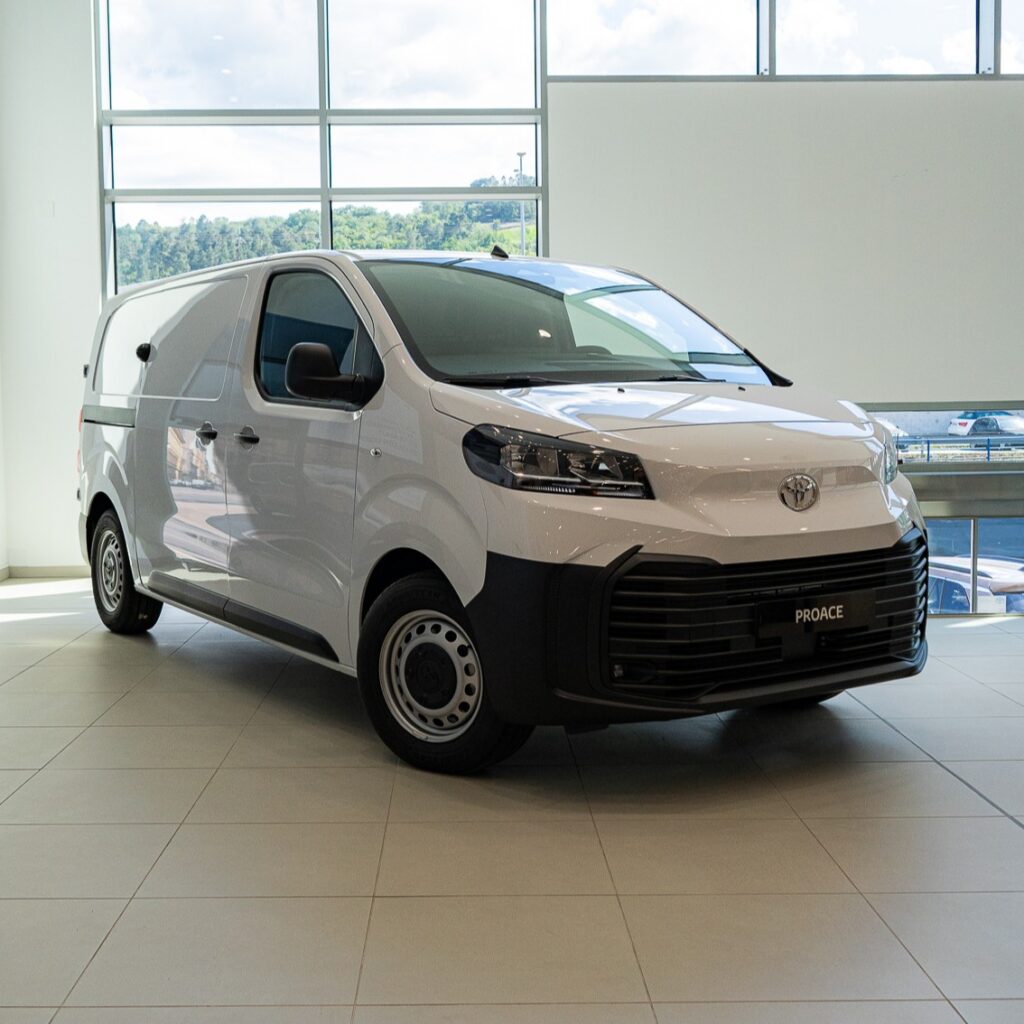 White Toyota Proace van on a showroom floor with large windows behind it.