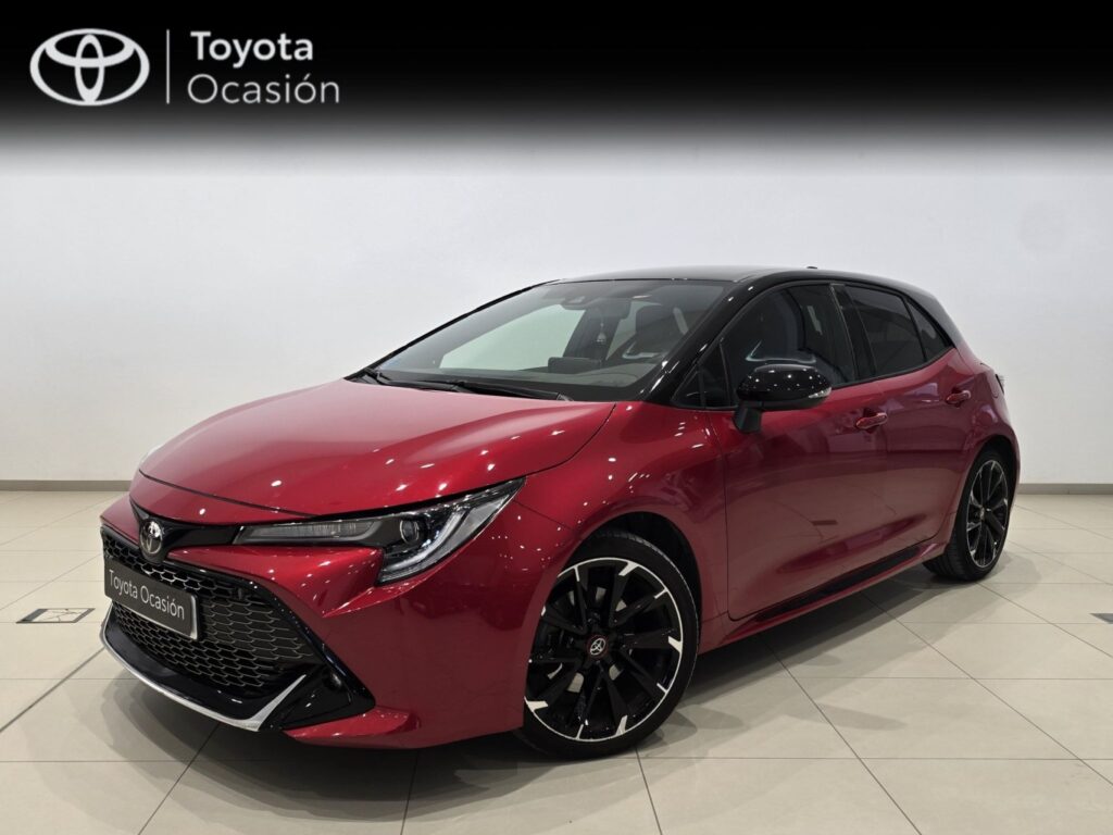 Red Toyota hatchback shown in a showroom with a black roof and large black alloy wheels, front-left 3/4 view, 'Toyota Ocasión' sign in the background
