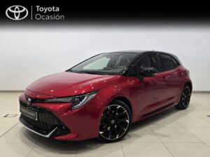 Red Toyota hatchback shown in a showroom with a black roof and large black alloy wheels, front-left 3/4 view, 'Toyota Ocasión' sign in the background